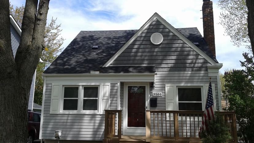 Modern craftsman-style house with wooden porch and American flag, surrounded by trees.