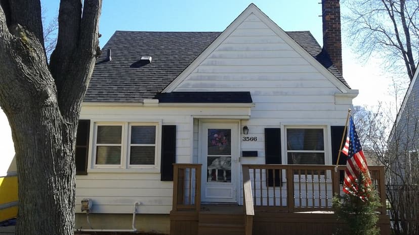 Charming white cottage with a porch, black shutters, and an American flag on display.